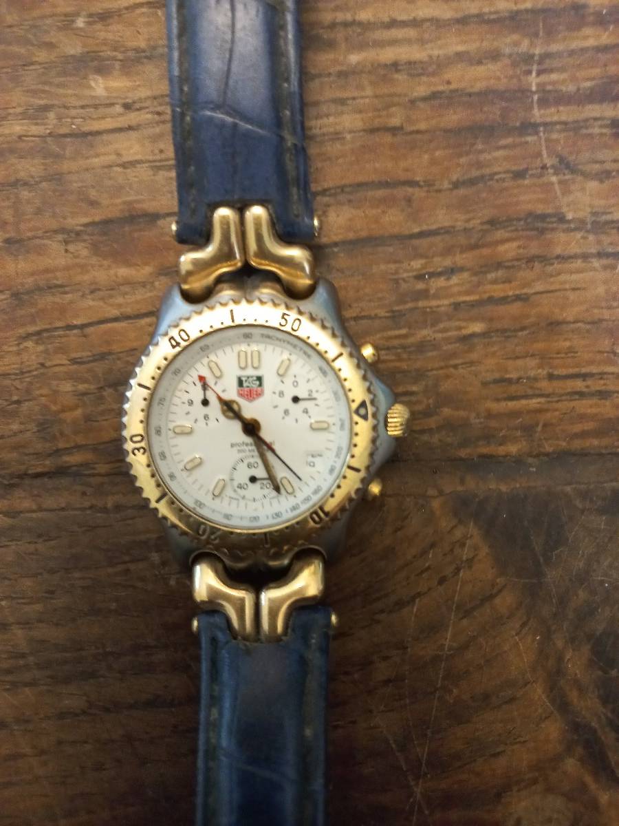 Vends montres tag heure boîtier en acier couronne dorée à la fin bracelet cuir bleu fond blanc