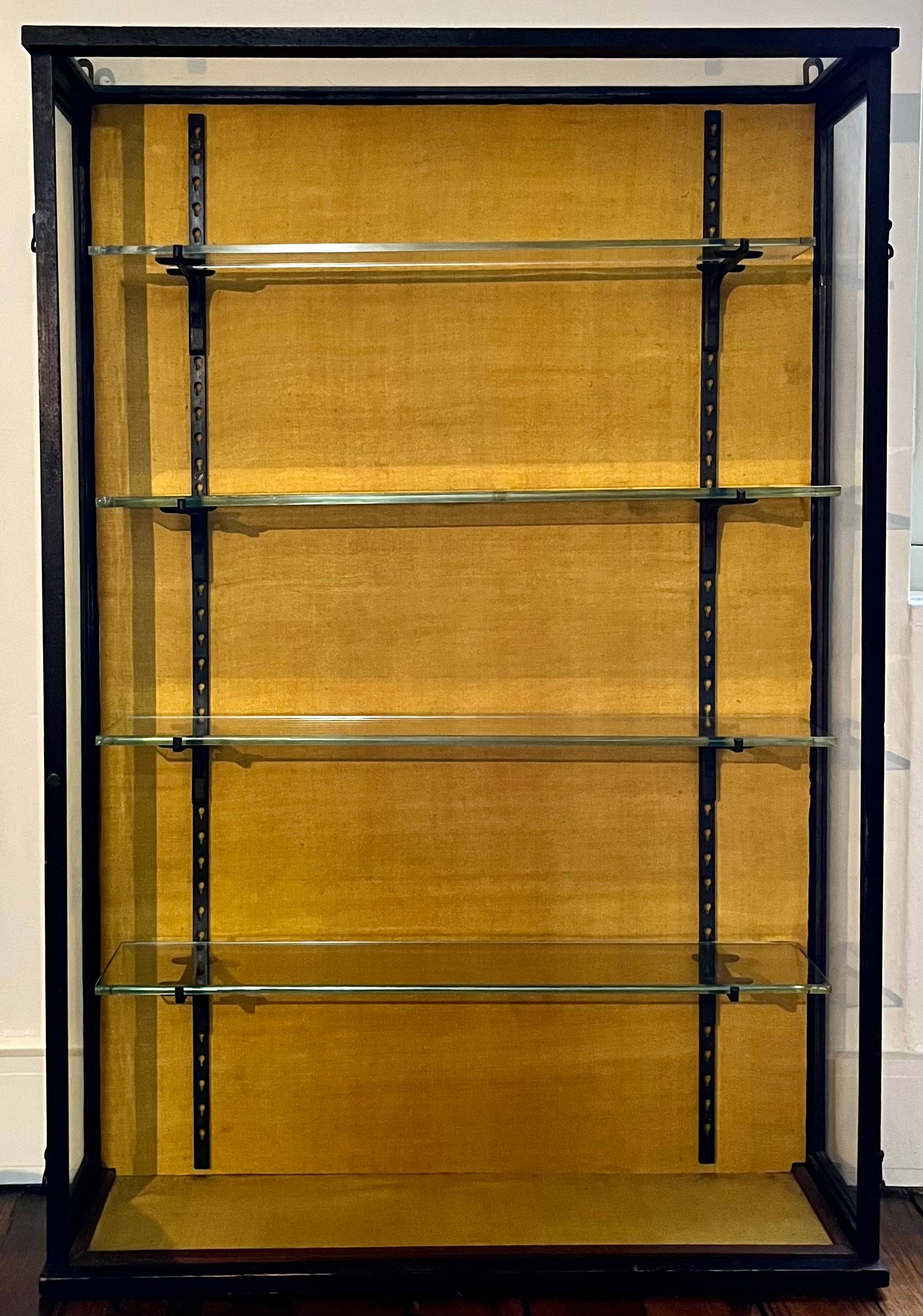 Vitrine de présentation en bois noirci à fond de tissu jaune moutarde, avec un verre ancien